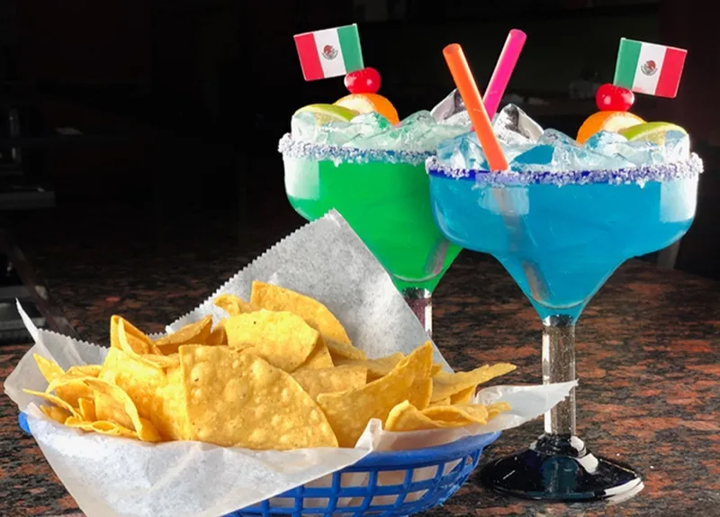 Green and blue margaritas with a basket of tortilla chips