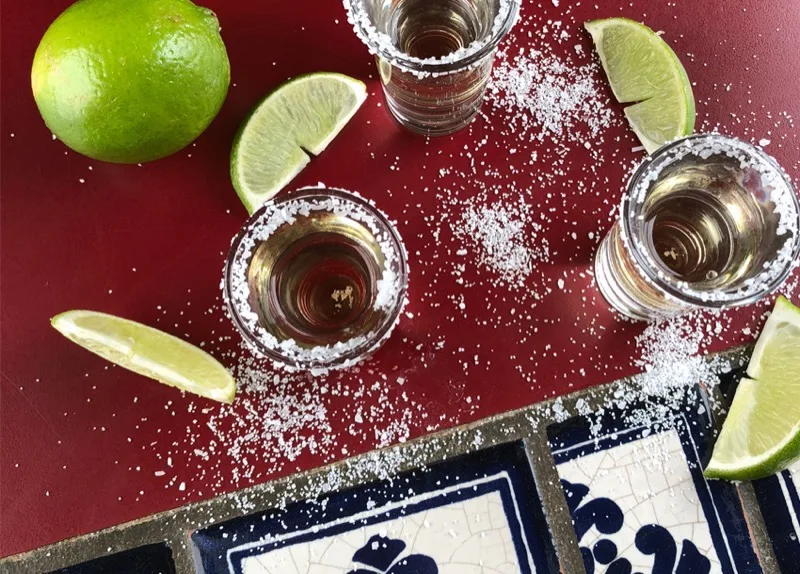 Tequila shots with lime and salt on a Talavera tile bar top