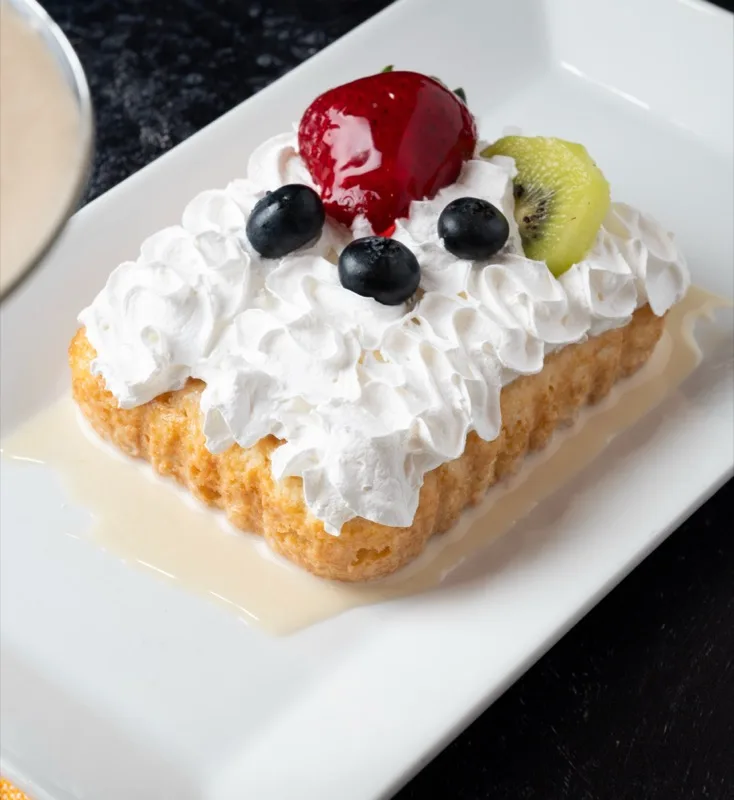 Tres leches cake topped with whipped cream, berries, and kiwi